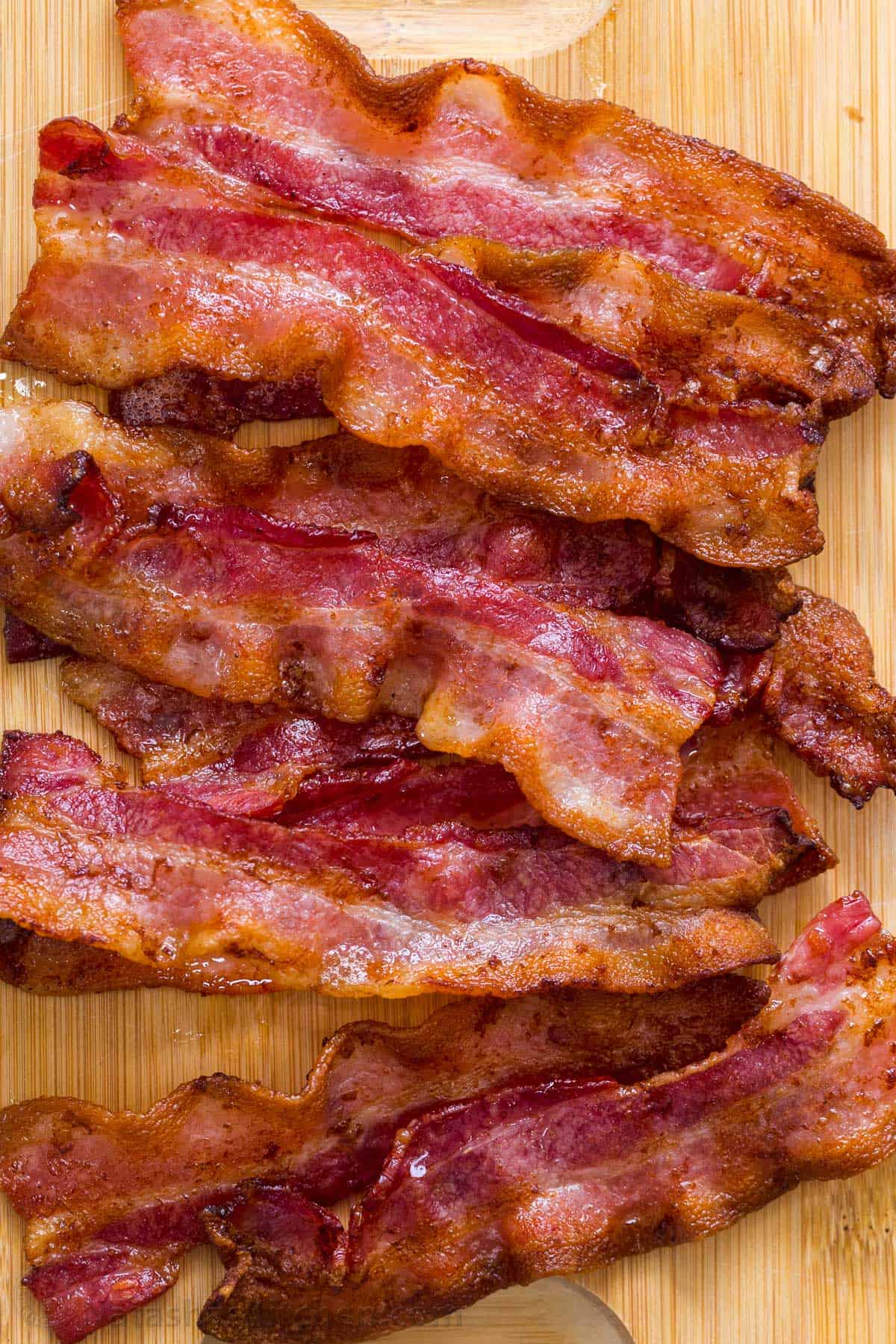 Recipe for how to cook bacon in the air fryer in just 10 minutes. Crispy and crunchy bacon slices cooked to perfection with less mess! Crispy cooked bacon laid out on a cutting board.