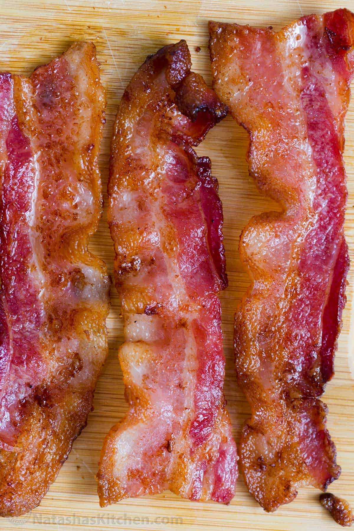 An EASY recipe for how to cook bacon in an air fryer to get crispy and flavorful bacon strips in only 10 minutes! Three slices of crispy cooked bacon laid out on a cutting board.