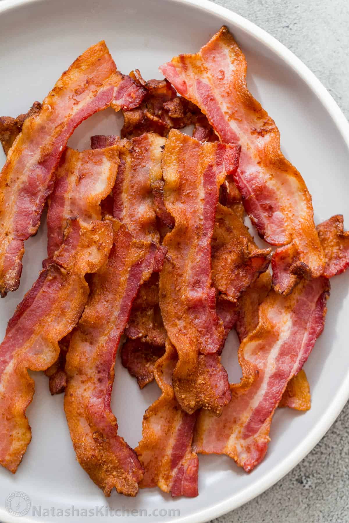 The BEST recipe for crispy air fryer bacon recipe that is ready in just 10 minutes. This bacon is great for breakfast, side dishes, toppings or even as a snack! Crispy air fryer bacon on a white plate stacked on top of each other.