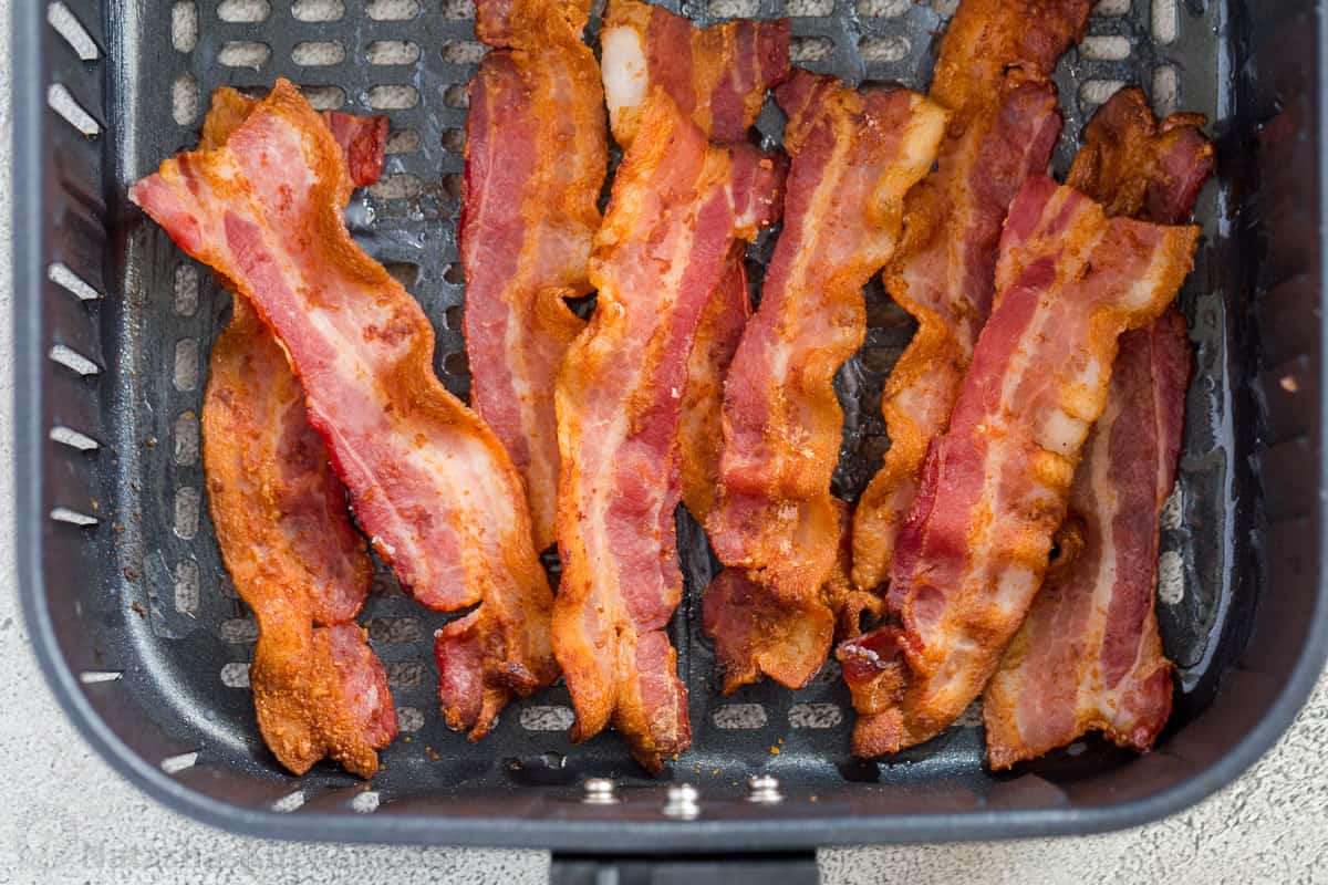 The air fryer recipe is so much easier to make, is less messy than the classic stove top or baked version and cooks quicker. Crunchy bacon strips laid out in an air fryer basket.