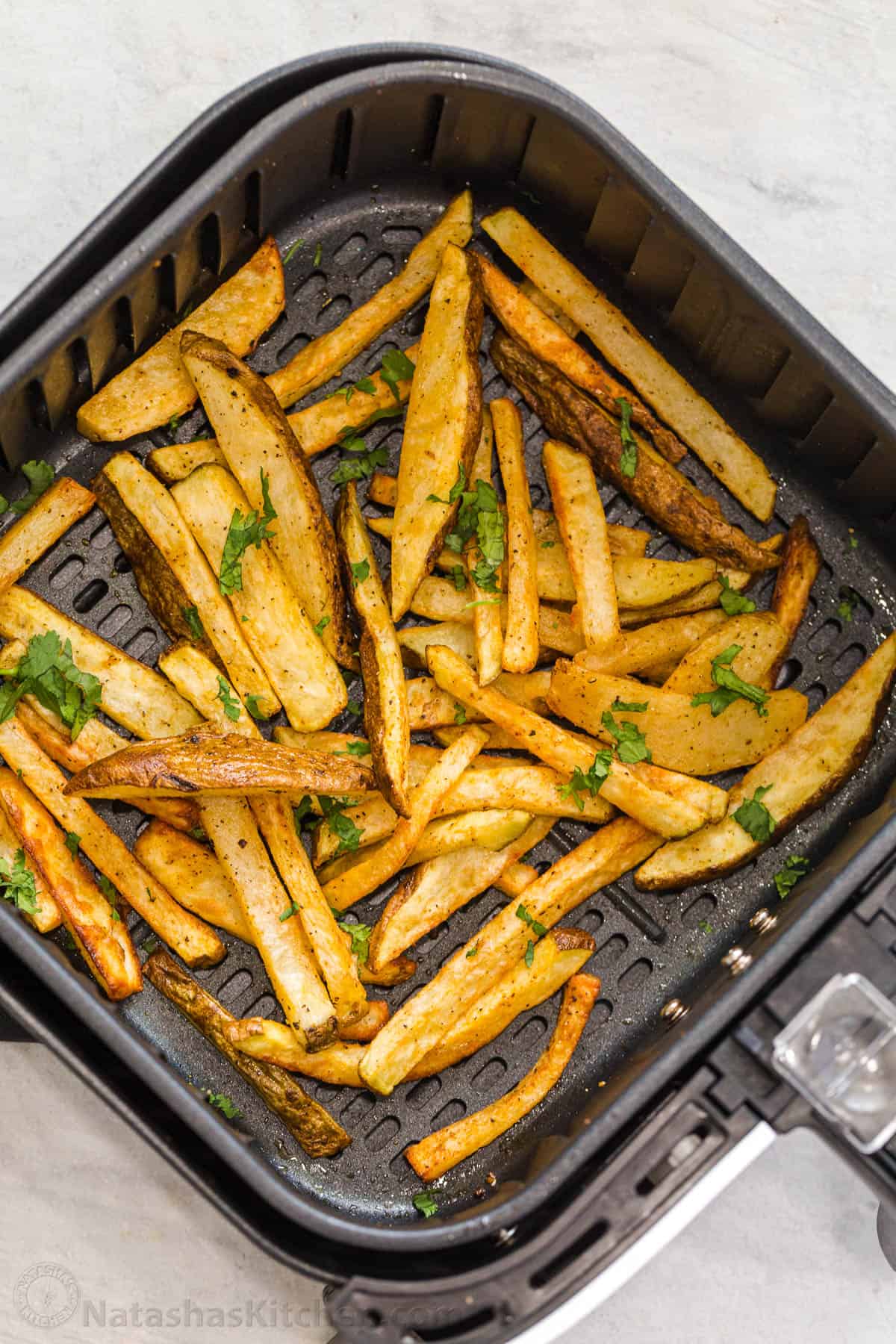 With just a few basic ingredients you can have homemade french fries ready without all the mess and grease of classic fried fries! Crispy French fries in an air fryer basket topped with fresh greens.