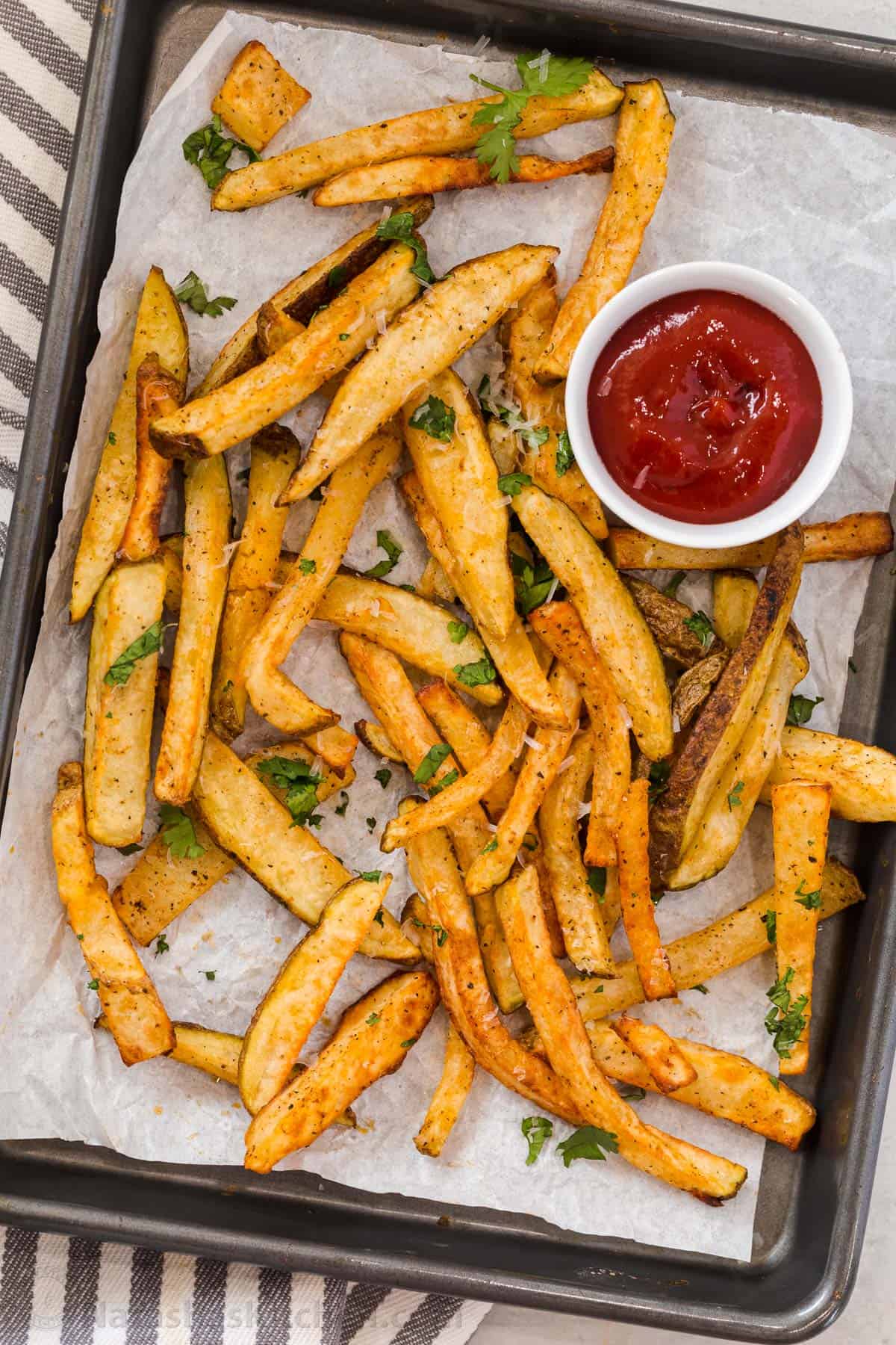 The BEST homemade crispy and crunchy air fryer French fries that are ready in under 30 minutes! Homemade crispy French fries on a baking sheet topped with chopped parsley and parmesan.
