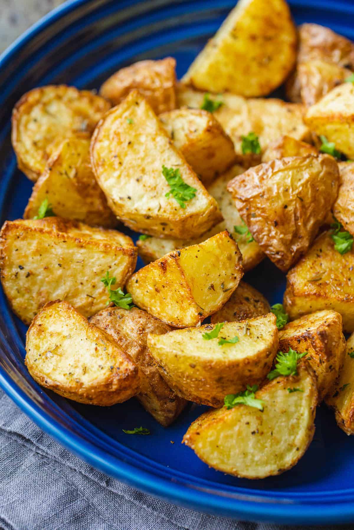 Close up of air fryer roasted potatoes on a blue platter, garnished with parsley.