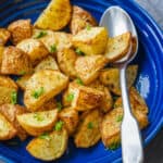 Air fryer roasted potatoes on a blue platter with a metal spoon, garnished with parsley.