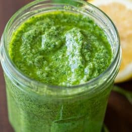 Pesto recipe in a glass jar with basil and lemon in the background