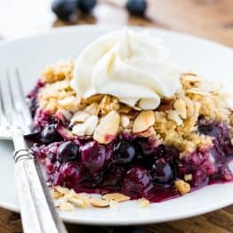 A plate and fork with a slice of blueberry crumble and whipped cream on it