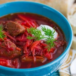 A bowl of borscht with meat garnished with sour cream and dill in a blue bowl