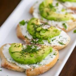 Four canapés with garlic herb cream cheese and avocado in a roll on a plate