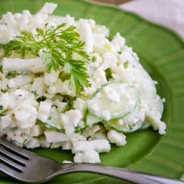 A green plate with cauliflower cucumber salad with a fork beside it