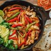 Chicken fajitas served out of a skillet with tortillas and sauces