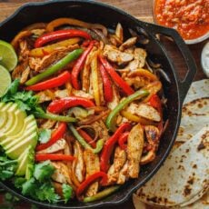 Chicken fajitas served out of a skillet with tortillas and sauces