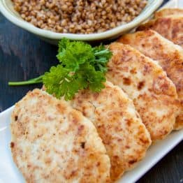 A plate of chicken kotleti lined up in a row with a bowl of buckwheat behind it