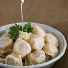 A white bowl of Russian chicken pelmeni with butter being poured over the top of them