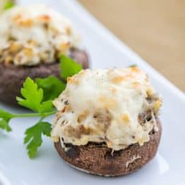 Three chicken stuffed mushrooms in a row on a long plate