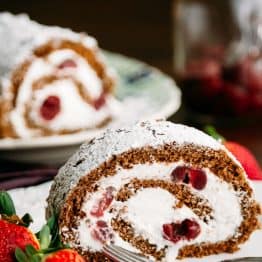 A slice of chocolate cherry roll with rum cream with the whole roll in the background