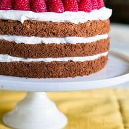 A close up of chocolate layer cake with creme chantilly frosting garnished with raspberries