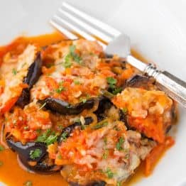 A white plate topped with eggplant with red pepper sauce and a fork beside it