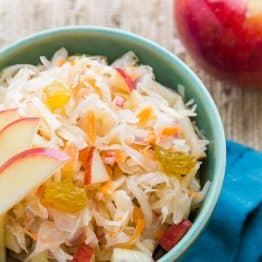 A green bowl of sauerkraut garnished with apples