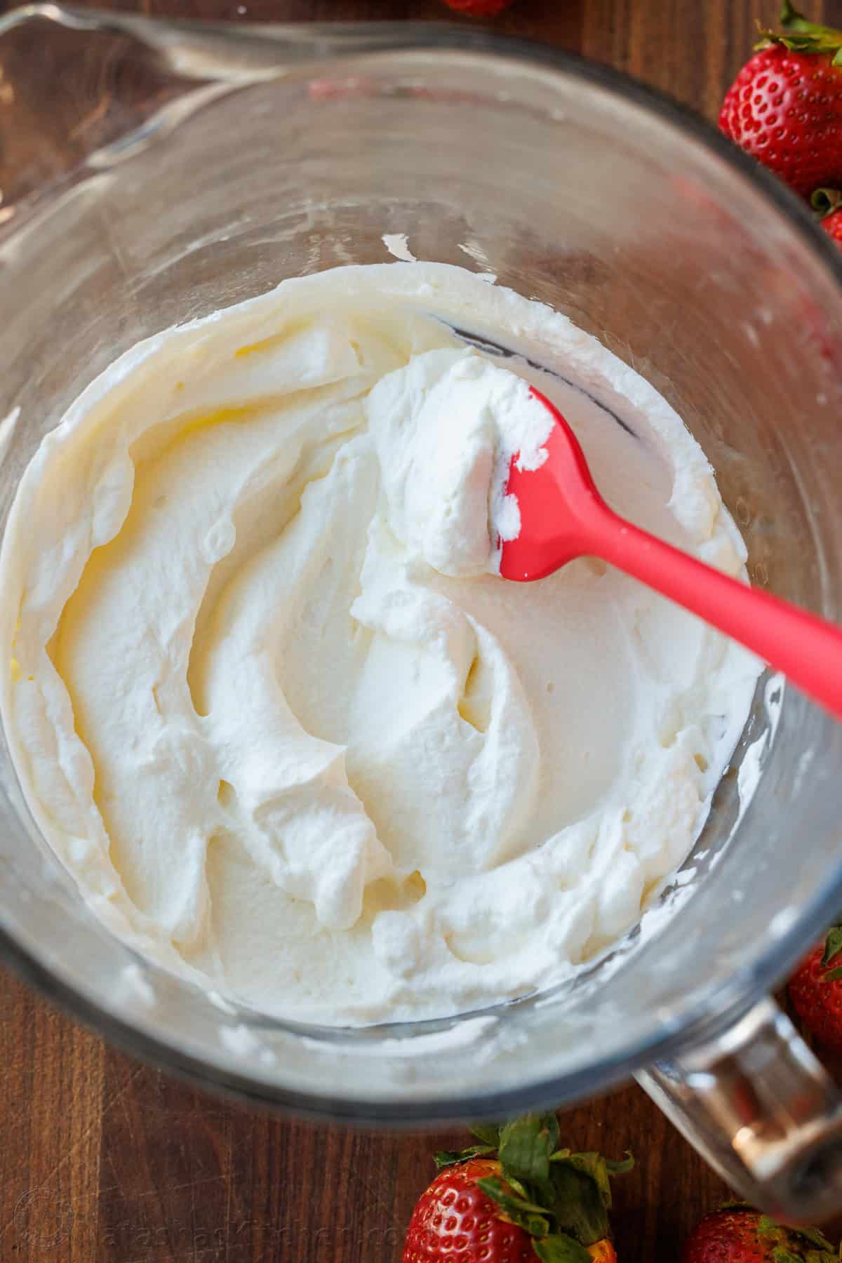 Make the Best Homemade Whipped Cream with 3 ingredients in minutes! Perfect for soft peaks or stiff peaks and to substitute store-bought topping. Homemade whipped cream recipe in a a mixing bowl with red spatula and strawberries around