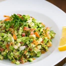 A bowl of loaded broccoli radish salad with a slice on lemon beside it