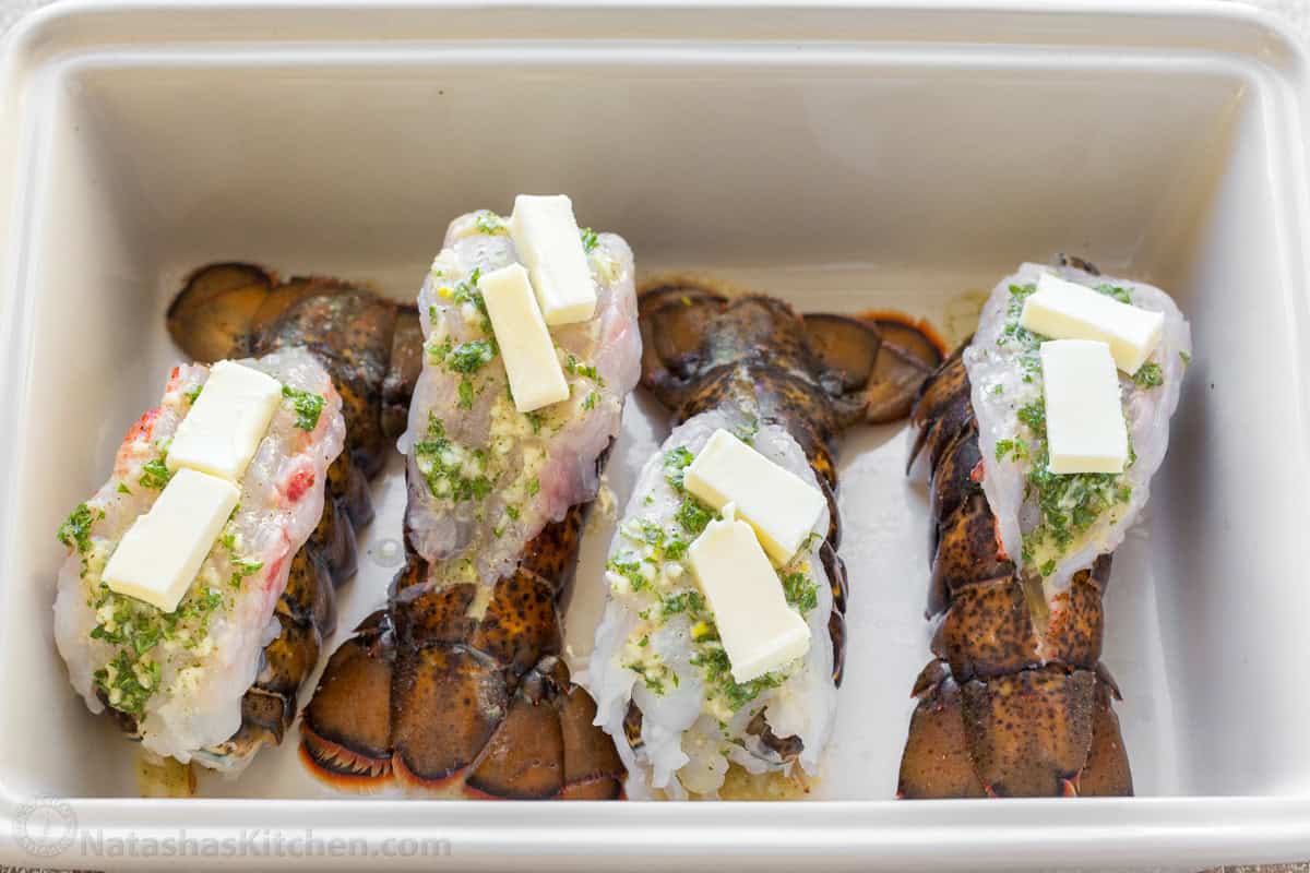 This Lobster Tail recipe with garlic butter sauce is juicy, flavorful, and easy. Includes an easy tutorial on how to butterfly lobster tail. Lobster tails butterflied and topped with sauce and butter in a baking dish.