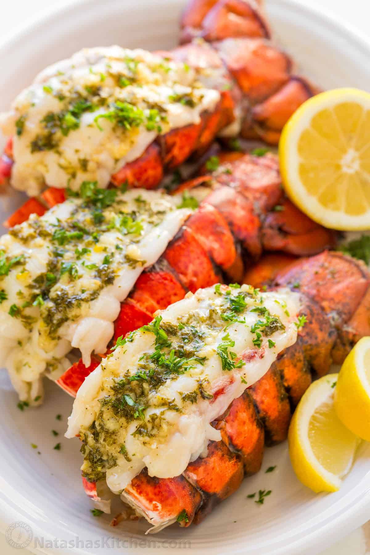 This Lobster Tail recipe with garlic butter sauce is juicy, flavorful, and easy. Includes an easy tutorial on how to butterfly lobster tail. Cooked lobster tails on a serving platter drizzled with lemon butter