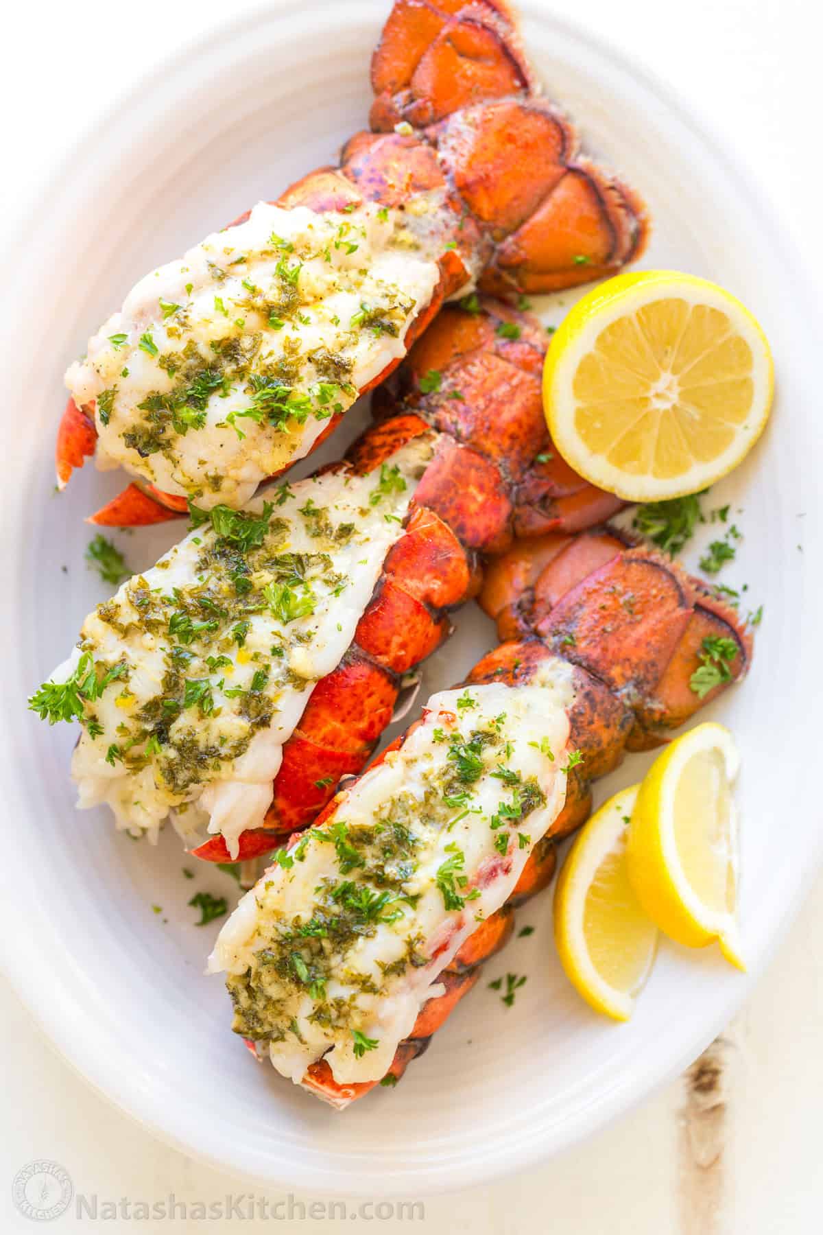This Lobster Tail recipe with garlic butter sauce is juicy, flavorful, and easy. Includes an easy tutorial on how to butterfly lobster tail. Lobster tails on a platter with lemon wedges