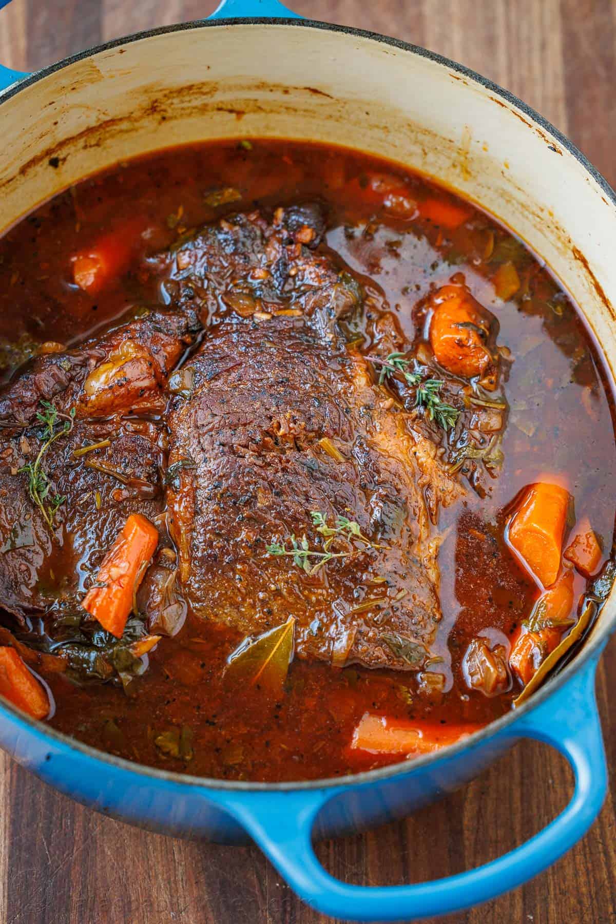 The best Pot Roast Recipe to get fall-apart tender beef with a rich sauce that doubles as a gravy. It will become your go-to comfort recipe! Chuck pot roast in a blue dutch oven with carrots and herbs