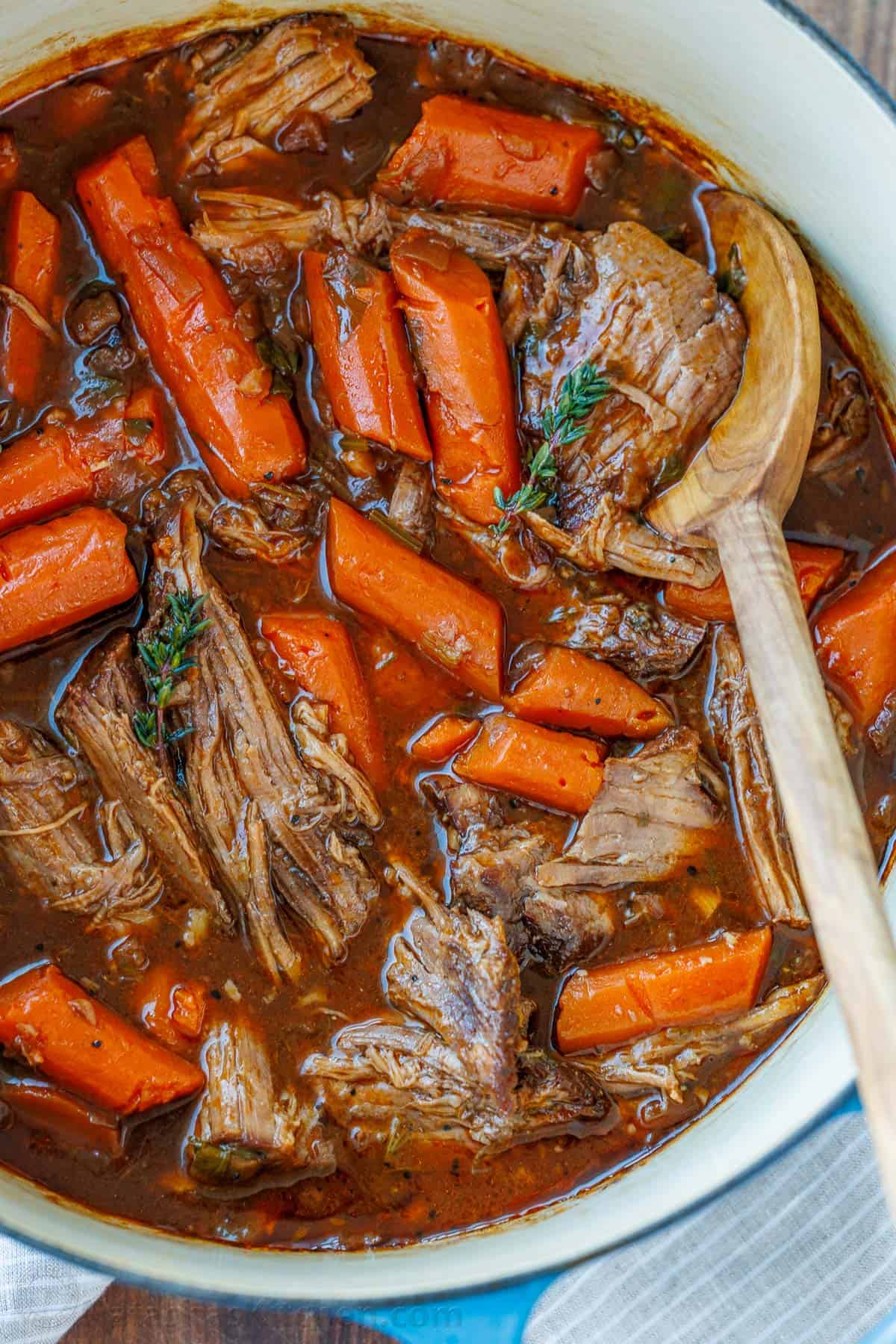 The best Pot Roast Recipe to get fall-apart tender beef with a rich sauce that doubles as a gravy. It will become your go-to comfort recipe! Cooked pot roast with carrots and thyme in a dutch oven with a wooden spoon