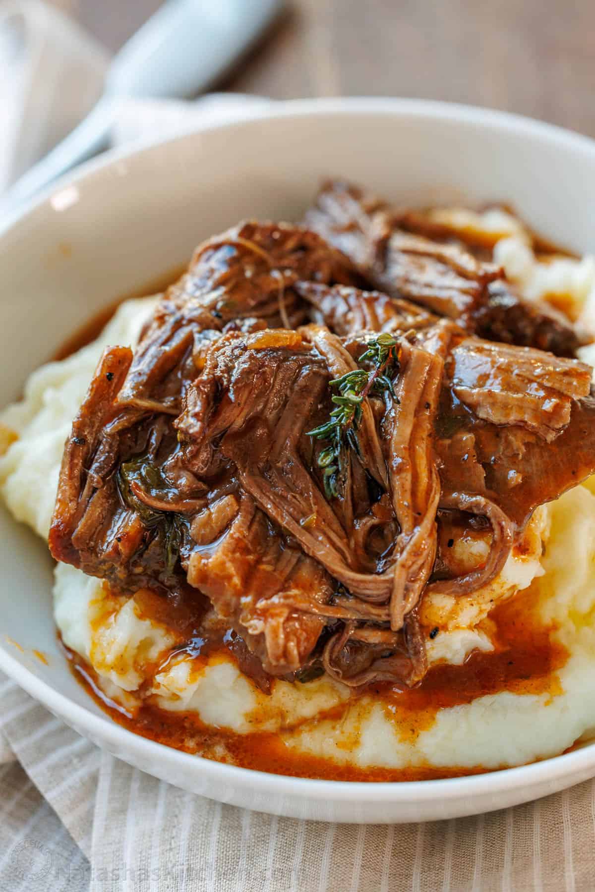 The best Pot Roast Recipe to get fall-apart tender beef with a rich sauce that doubles as a gravy. It will become your go-to comfort recipe! classic pot roast recipe served over mashed potatoes in a white bowl