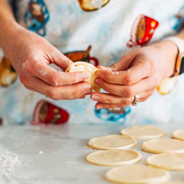 Pierogi filled with cheesy potatoes and served with crisp bacon, melted butter and sour cream. Homemade Pierogi is the ultimate comfort food! hands crimping the edges of pierogi dough