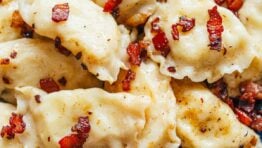 Cooked pierogies on a blue plate with bacon