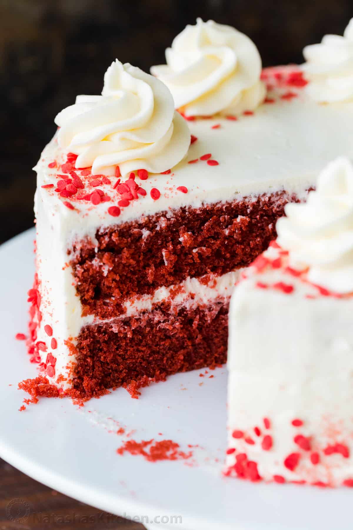 Our homemade Red Velvet Cake has a soft and moist crumb with the best Cream Cheese Frosting. Perfect for Valentine's, birthdays, or any special occasion. Red Velvet Cake cake on platter with one piece removed
