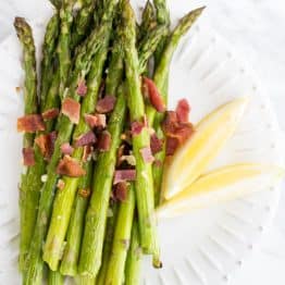 Roasted asparagus one a plate covered in bacon and lemon wedges on a plate
