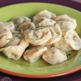 A green plate with Russian pelmeni garnished with dill