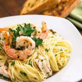 A plate of angel hair with lemon shrimp scampi with two toasted baguette slices behind the plate