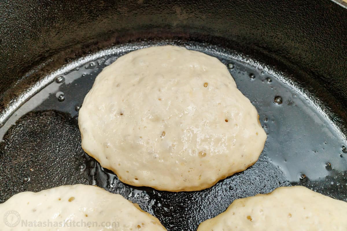 Overnight Sourdough Pancakes are easy! Mix everything before bed, leave at room temp overnight, and wake up to bubbly, ready-to-cook pancake batter. Sourdough Pancakes in a skillet, bubbling batter, indicates these pancakes are ready to flip.