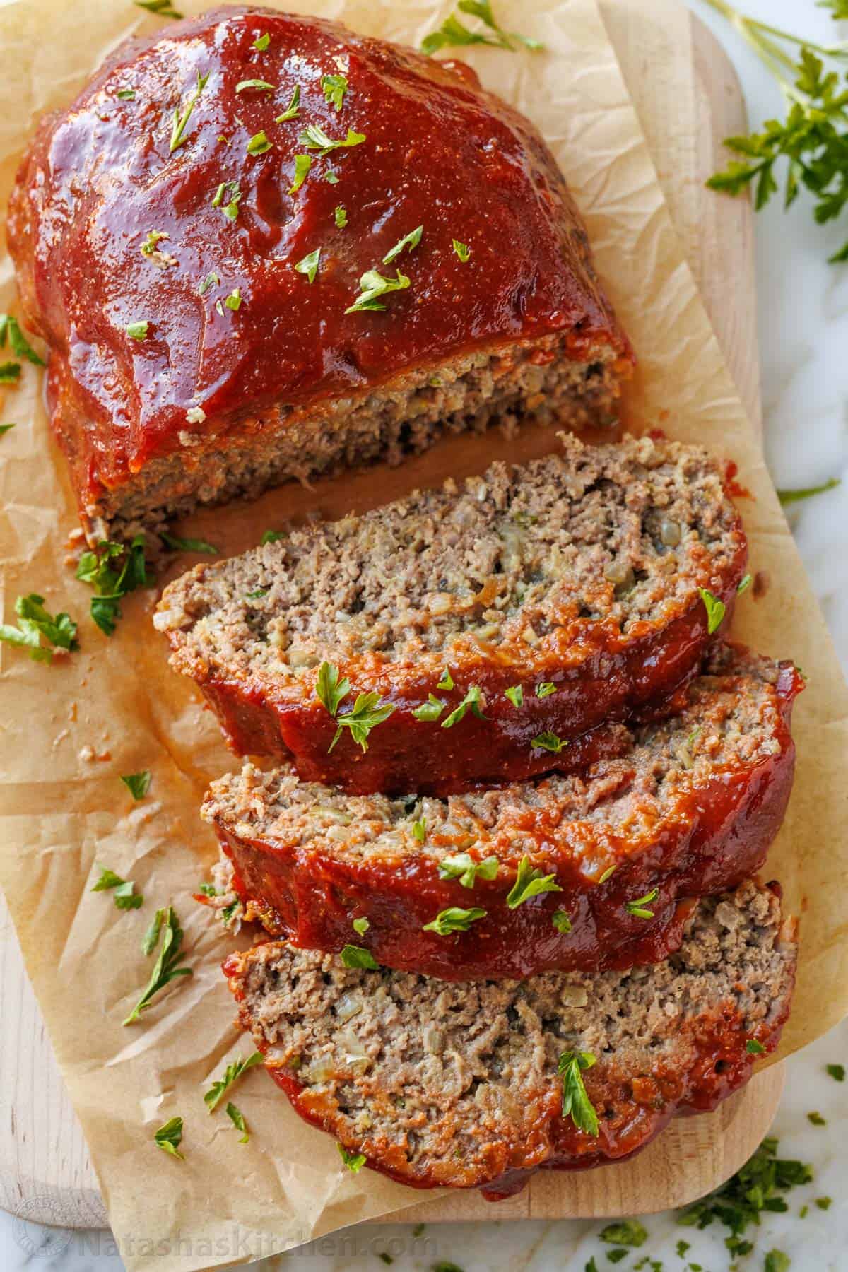 This is my favorite meatloaf recipe. The meatloaf is tender and juicy on the inside with a sweet and tangy glaze that adds so much flavor! Juicy sliced meatloaf on a cutting board garnished with parsley