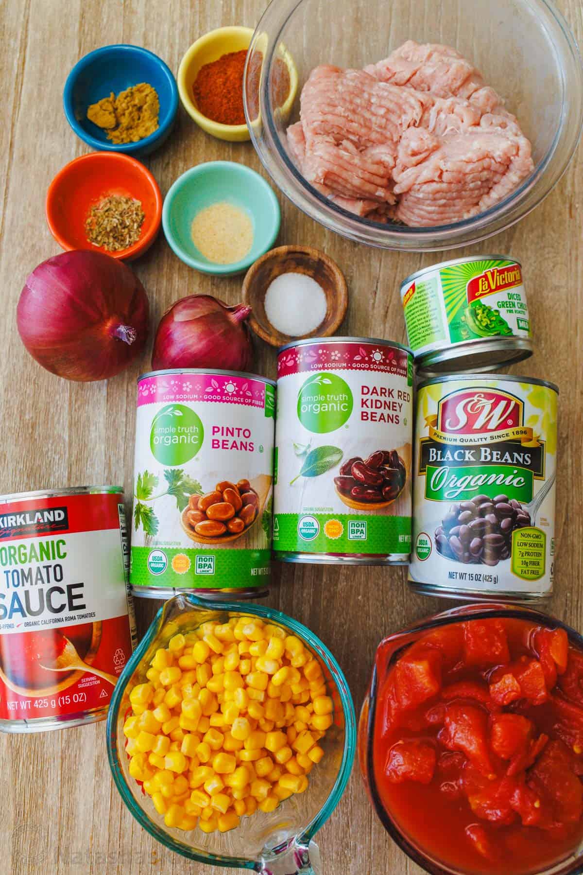 ingredients for turkey chili recipe including ground turkey, red onion, chili powder, cumin, garlic powder, oregano, salt, pepper, diced tomatoes, tomato sauce, black beans, kidney beans, pinto beans, green chilis, and corn